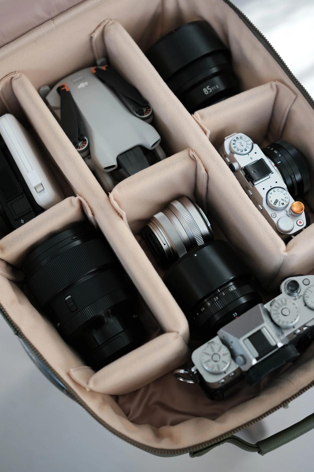 Camera equipment including lenses and bodies inside a beige compartmentalized bag.