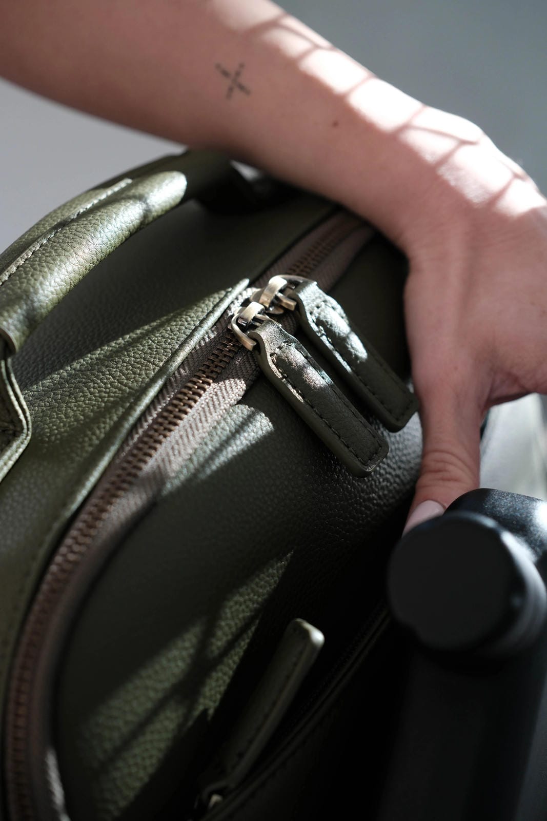 Hand zipping a green suitcase with a blurred background
