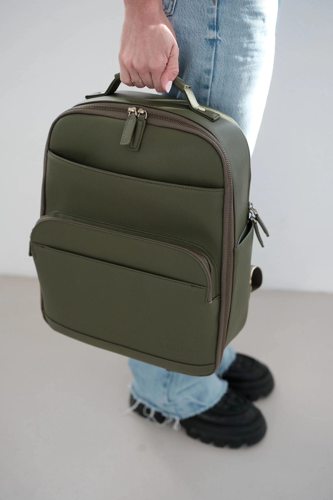 Person holding a green backpack against a neutral background