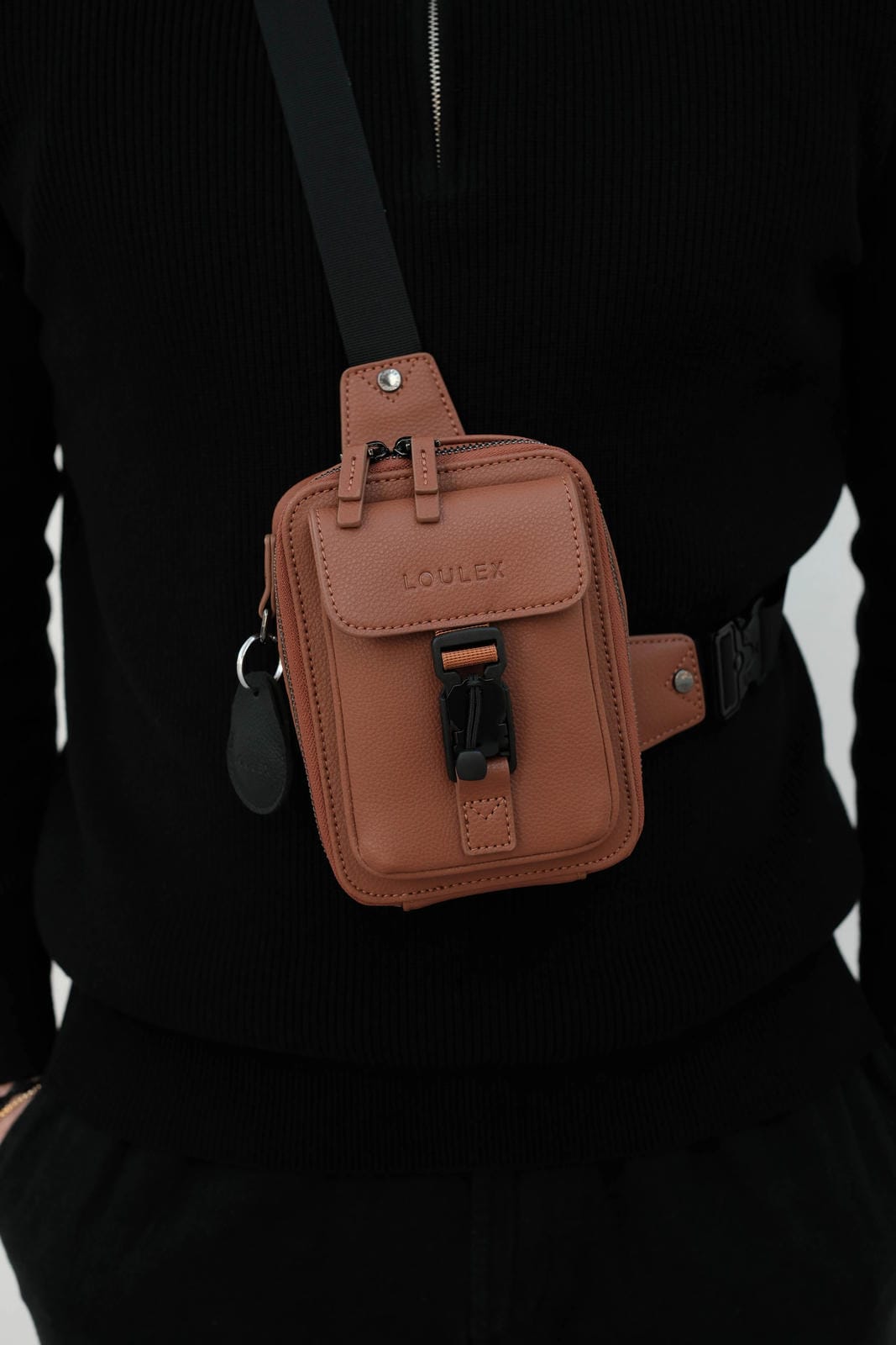 Brown leather waist bag worn by a person against a black background