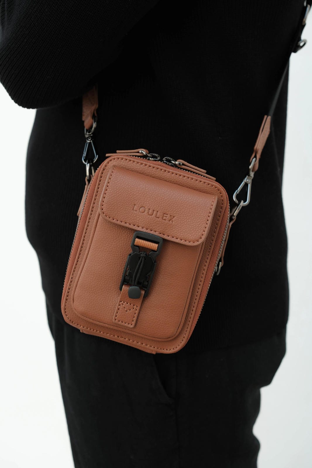 Brown leather crossbody bag with 'LOULEX' branding on a person wearing black clothing.