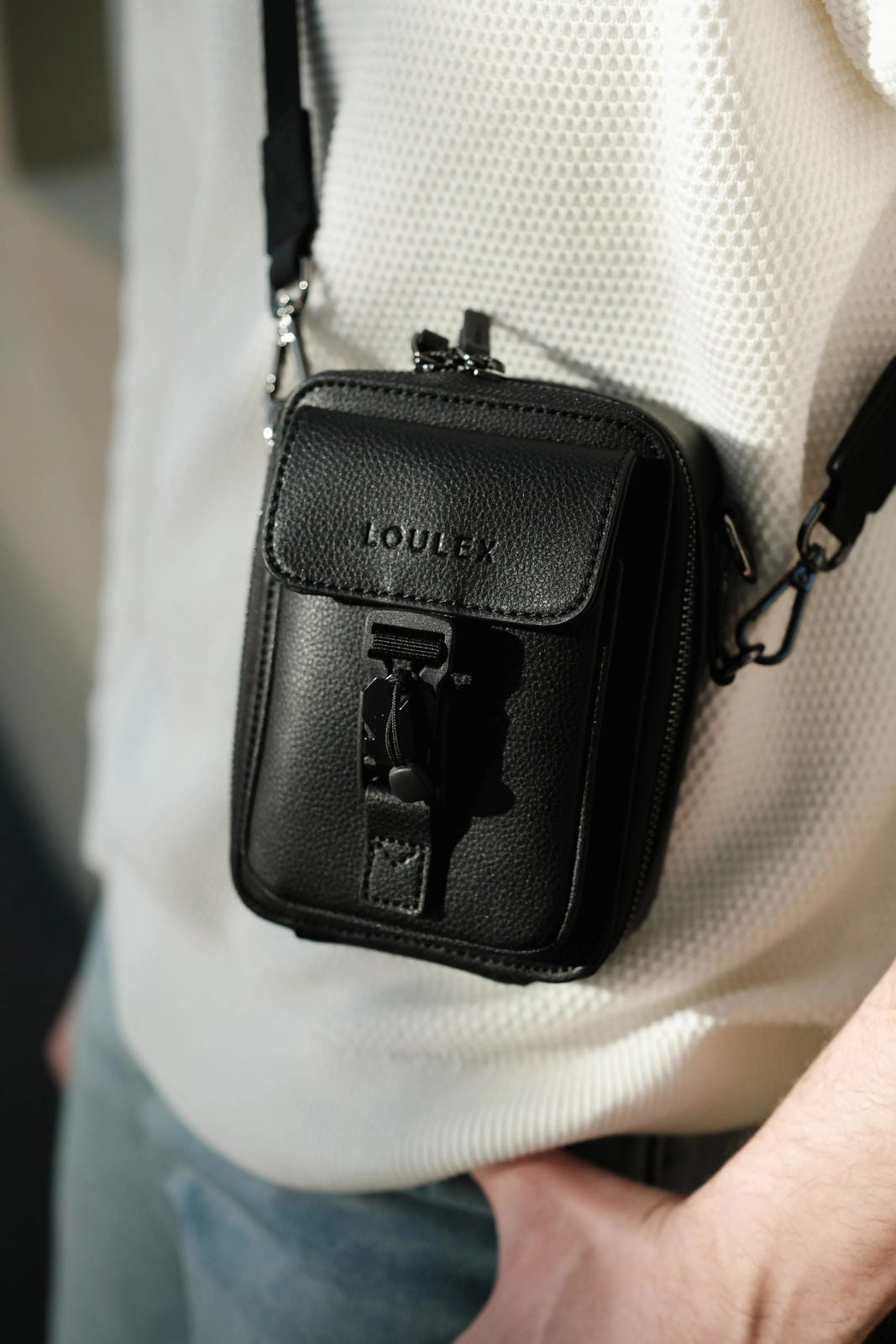 Black leather crossbody bag with 'LOU' brand logo worn by a person.