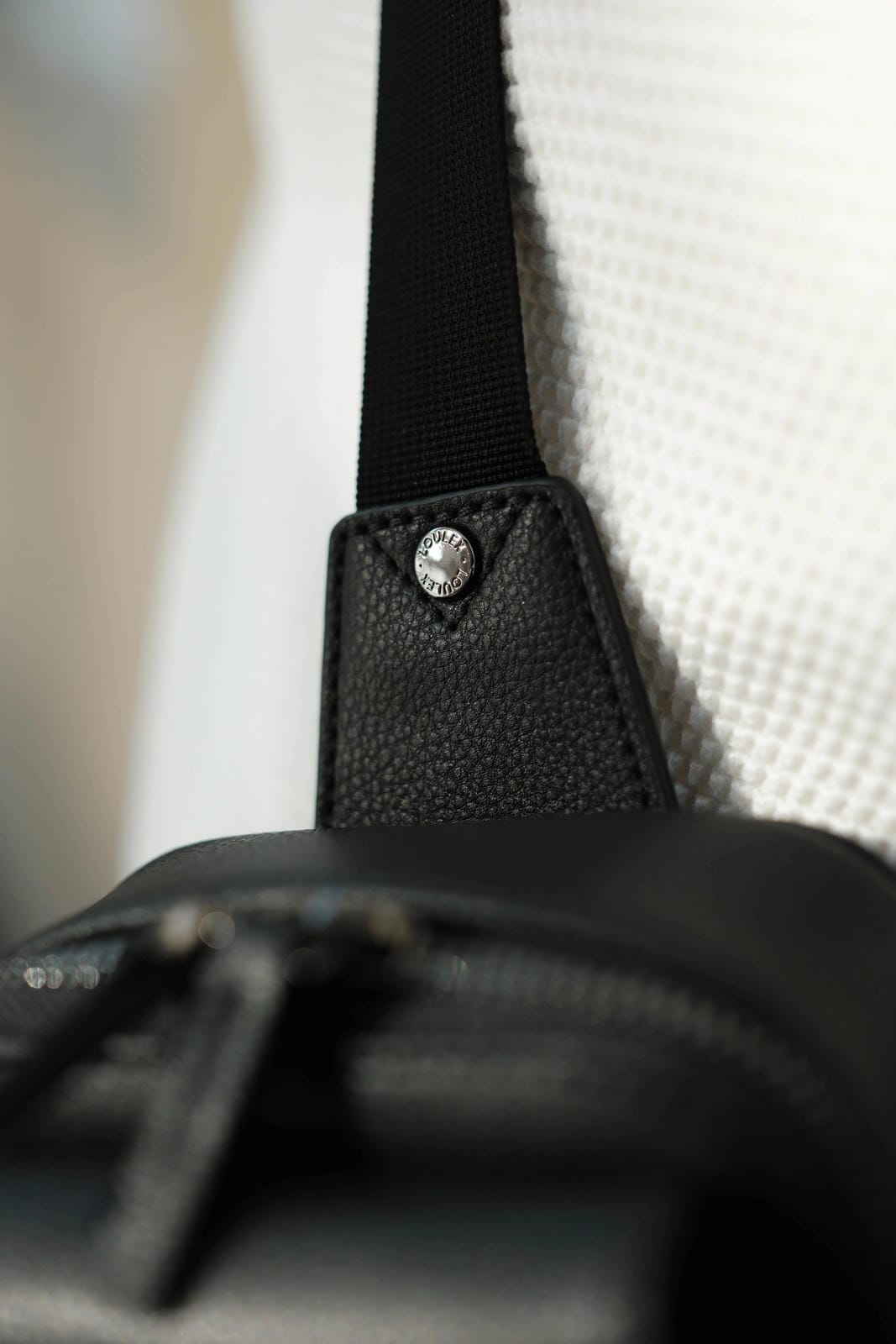 Close-up of a black leather bag with a strap and decorative button on a blurred background