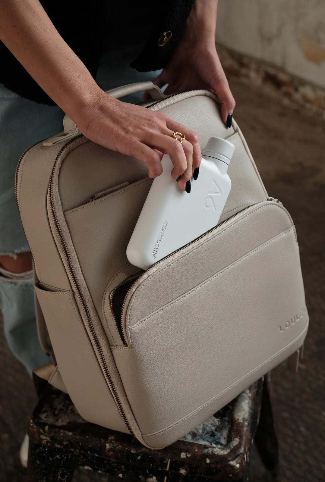 Beige backpack with a white bottle inside, held by a person.