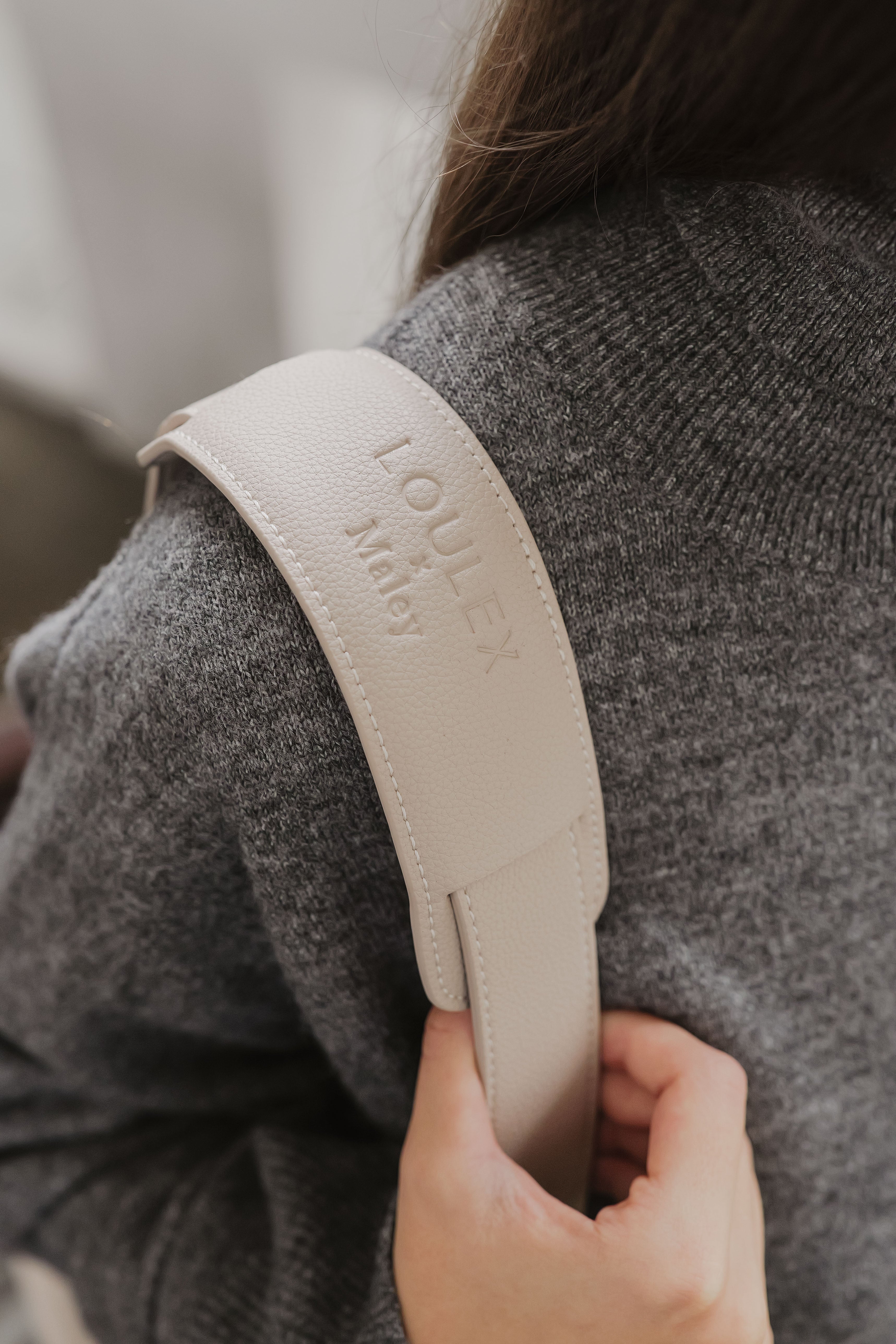Beige riem met 'LOULEX'-logo, vastgehouden door een persoon die een grijze trui draagt.