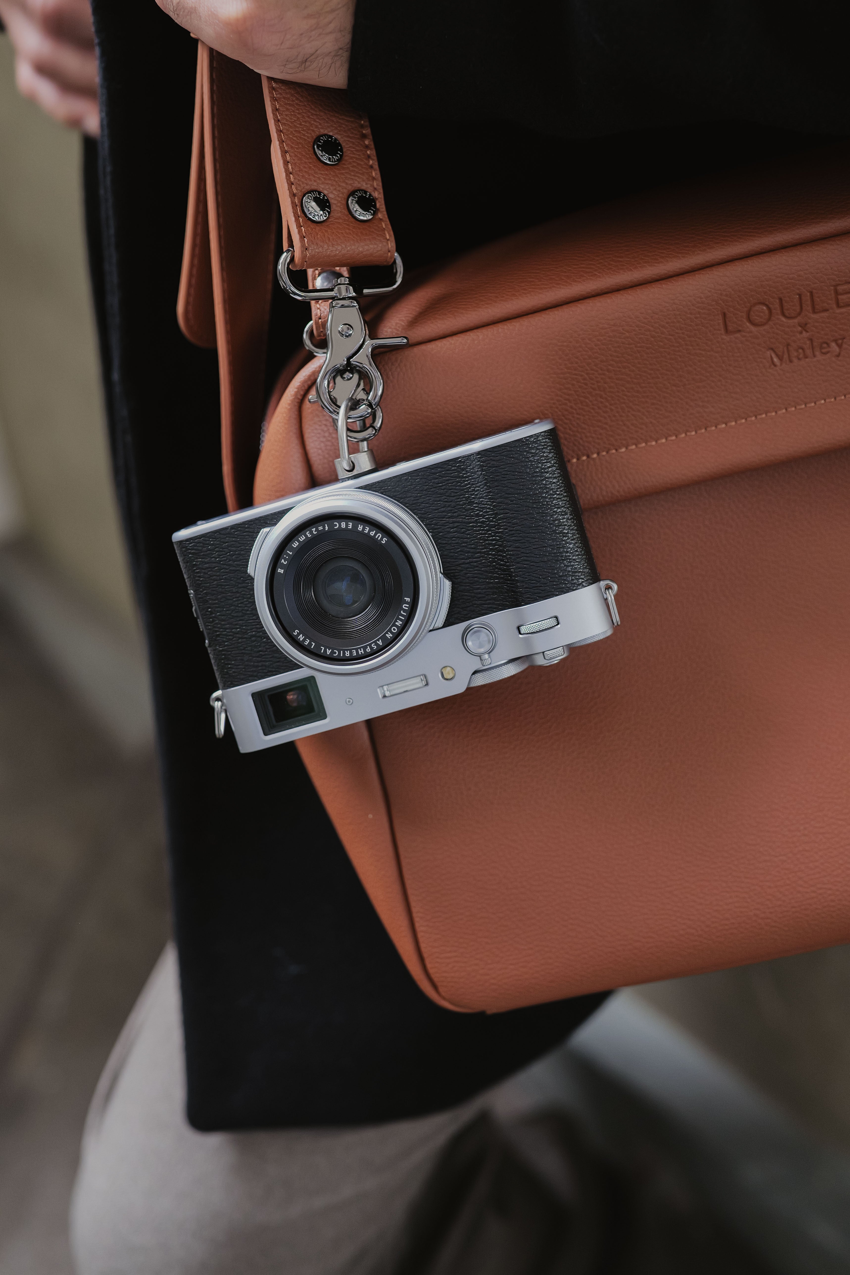 Camera-vormige sleutelhanger bevestigd aan een bruine leren tas