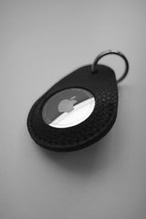 Funda negra para AirTag con manzana sobre fondo gris