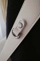 Primer plano de una correa de cuero beige con hebilla metálica sobre fondo negro.