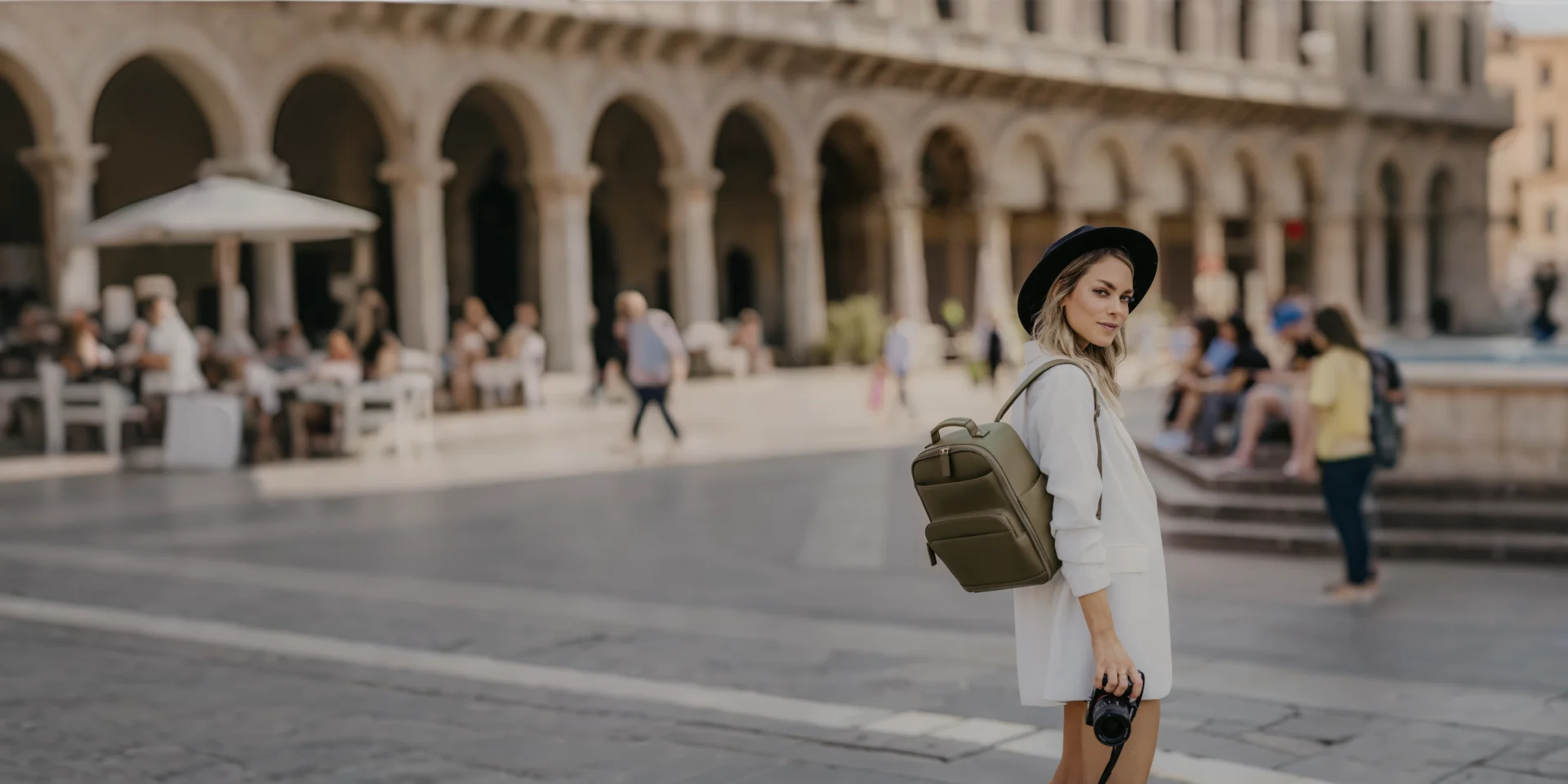 Woman with a backpack standing in an open square with architectural columns in the background