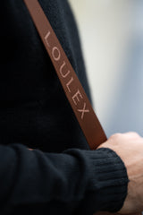 Cinturino marrone con marchio "LOULEX" tenuto da una persona che indossa un maglione nero.