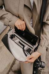 Persona che tiene una borsa con una macchina fotografica all'interno, indossando un cappotto.