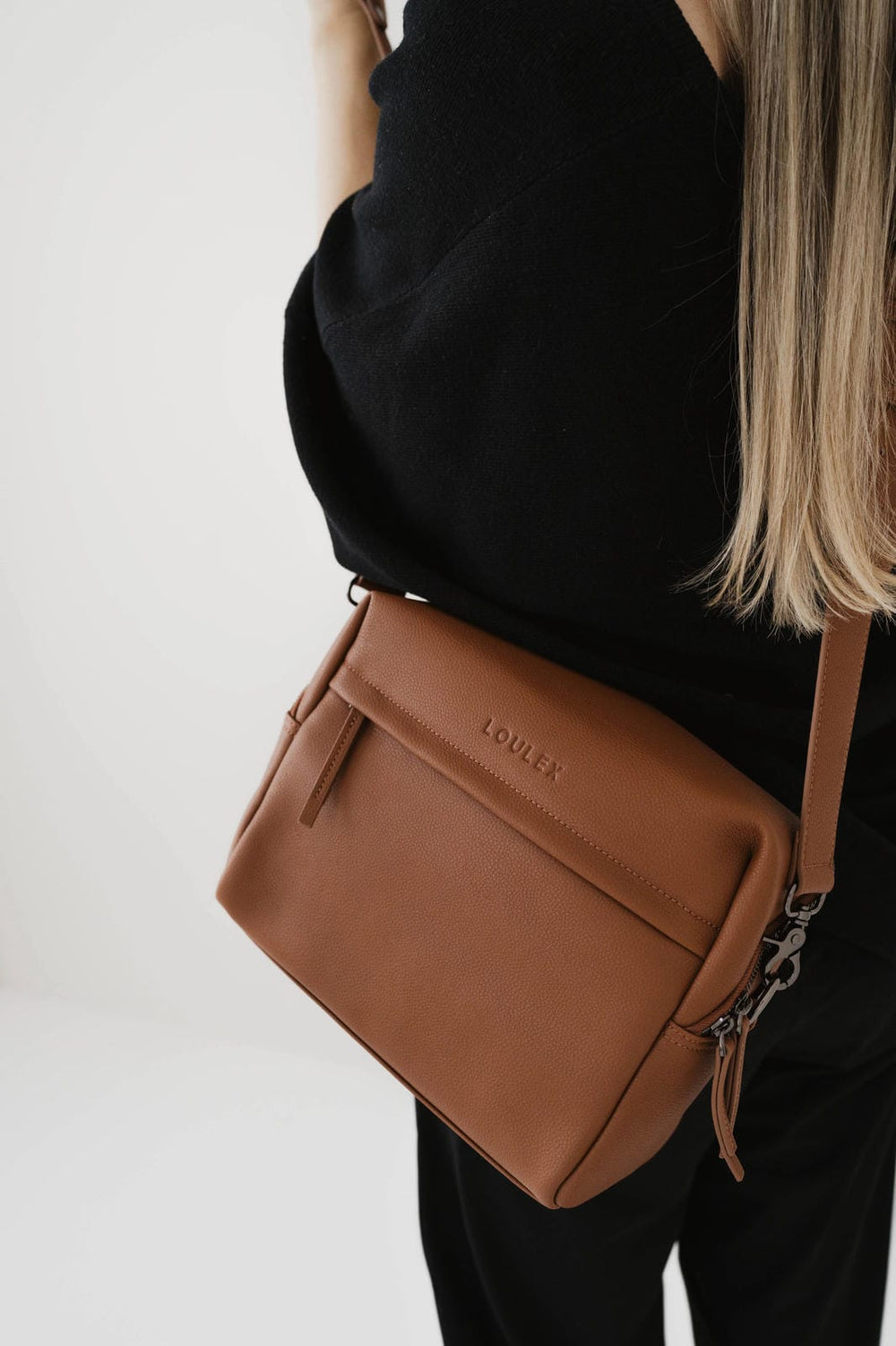 Borsa marrone con logo del marchio visibile indossata da una persona su sfondo bianco