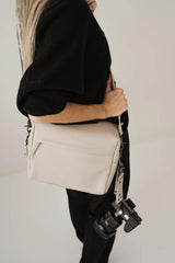 Persona che tiene in mano una borsa beige con logo del marchio visibile su sfondo semplice