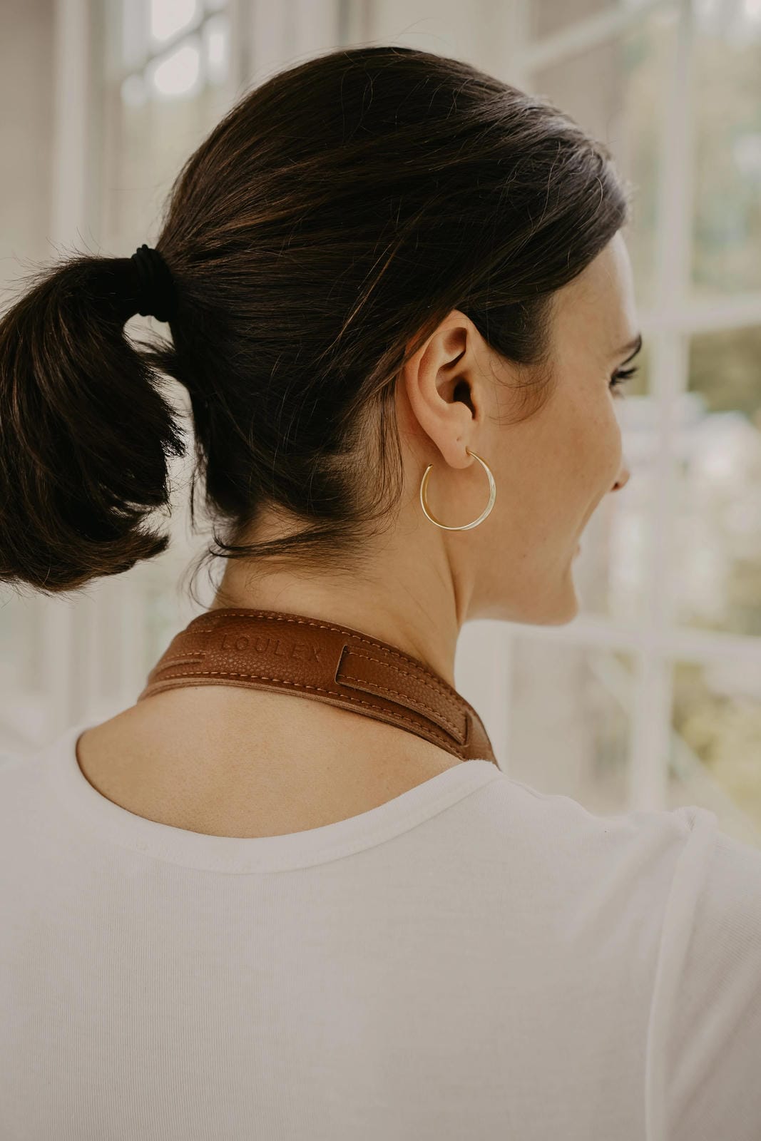 Femme portant des boucles d'oreilles créoles dorées sur fond flou