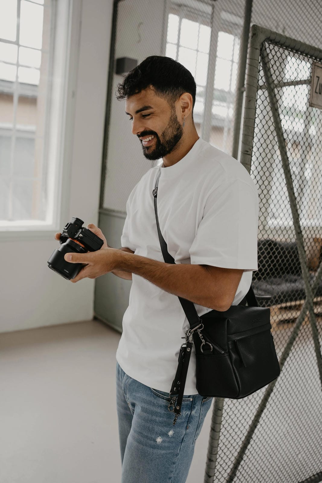 Man holding a camera and a black bag in an indoor setting