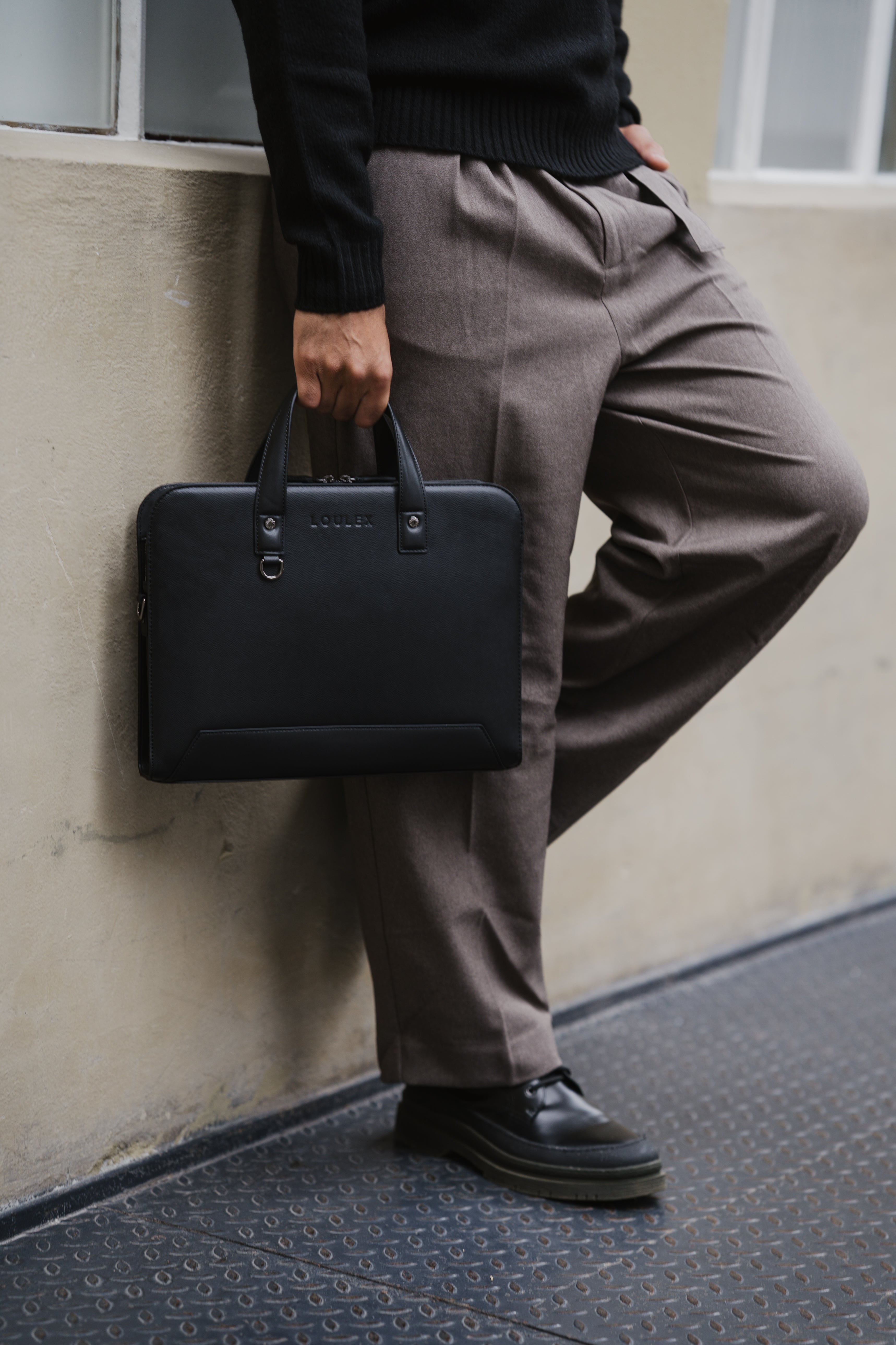 Person holding a black briefcase against a wall