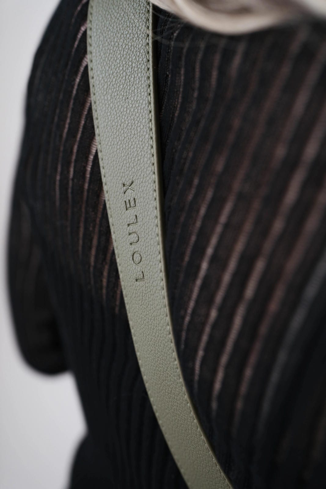 Close-up of a green leather strap with 'LOULEX' branding on a dark textured background.