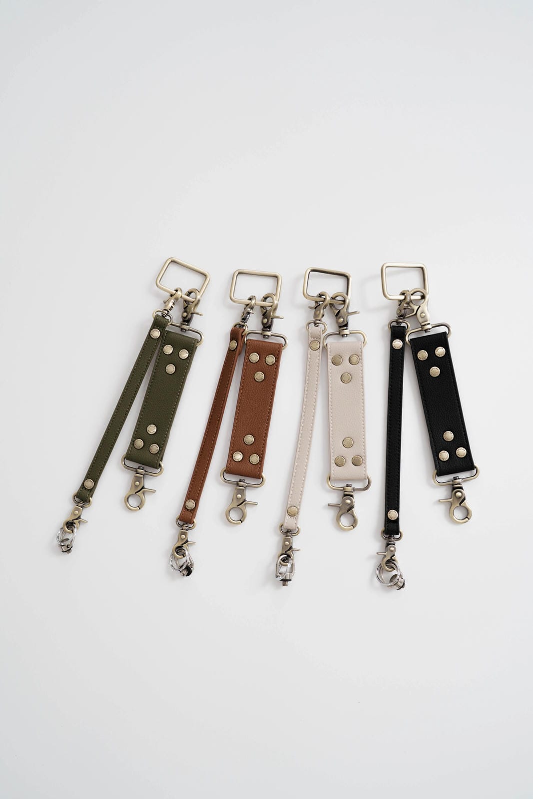 Five leather keychains with studded details on a white background