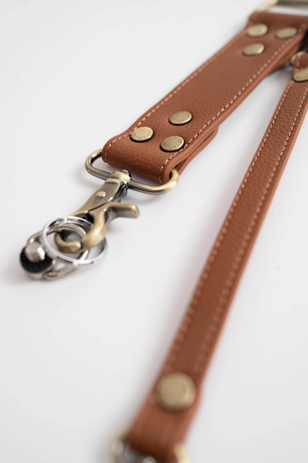 Brown leather strap with brass studs and a metal clasp on a white background