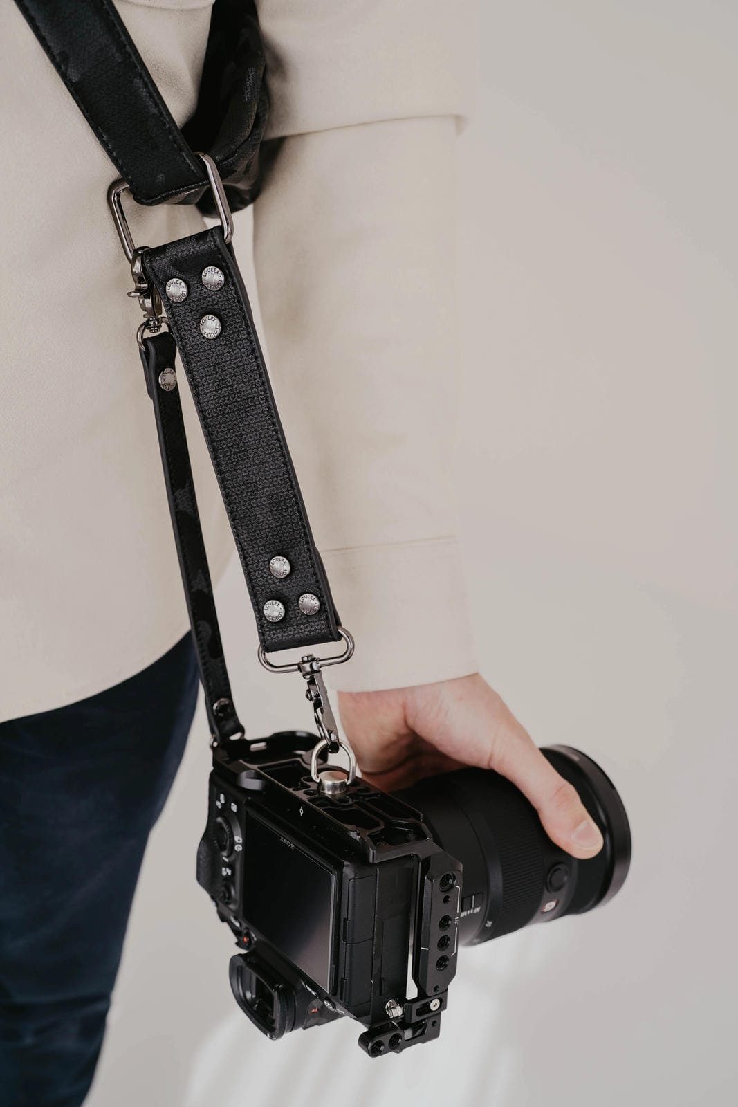 Person holding a camera with a black leather strap against a neutral background