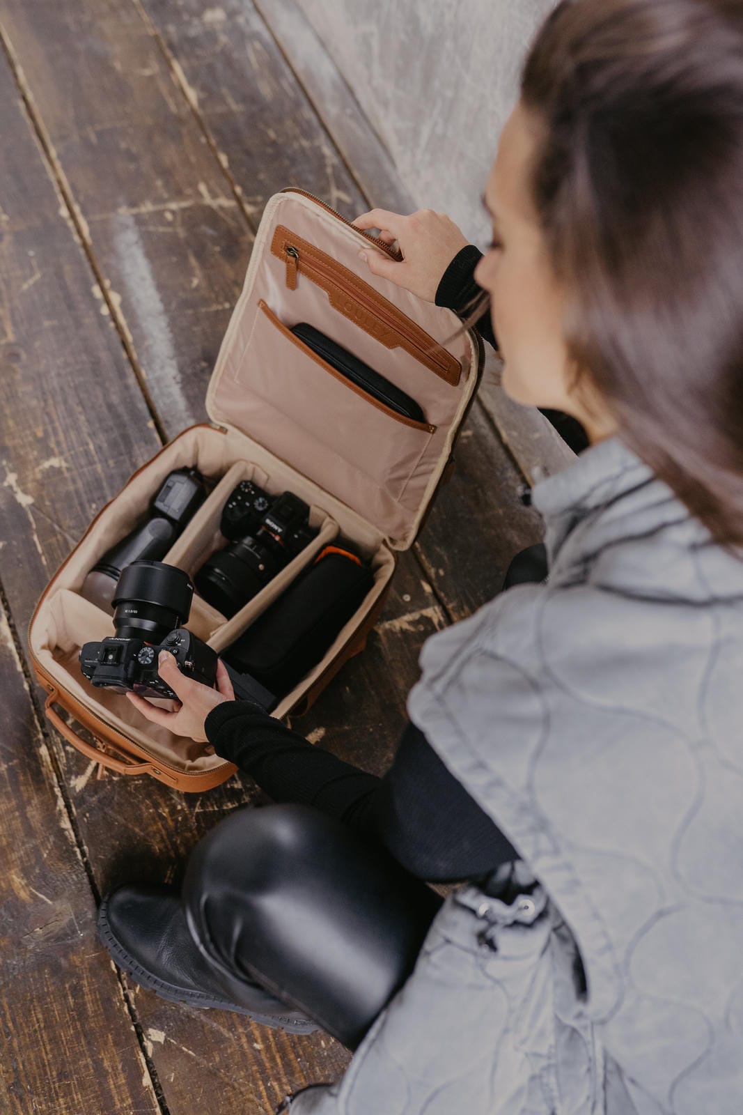 Personne rangeant du matériel photographique dans une valise de voyage beige posée sur une surface en bois