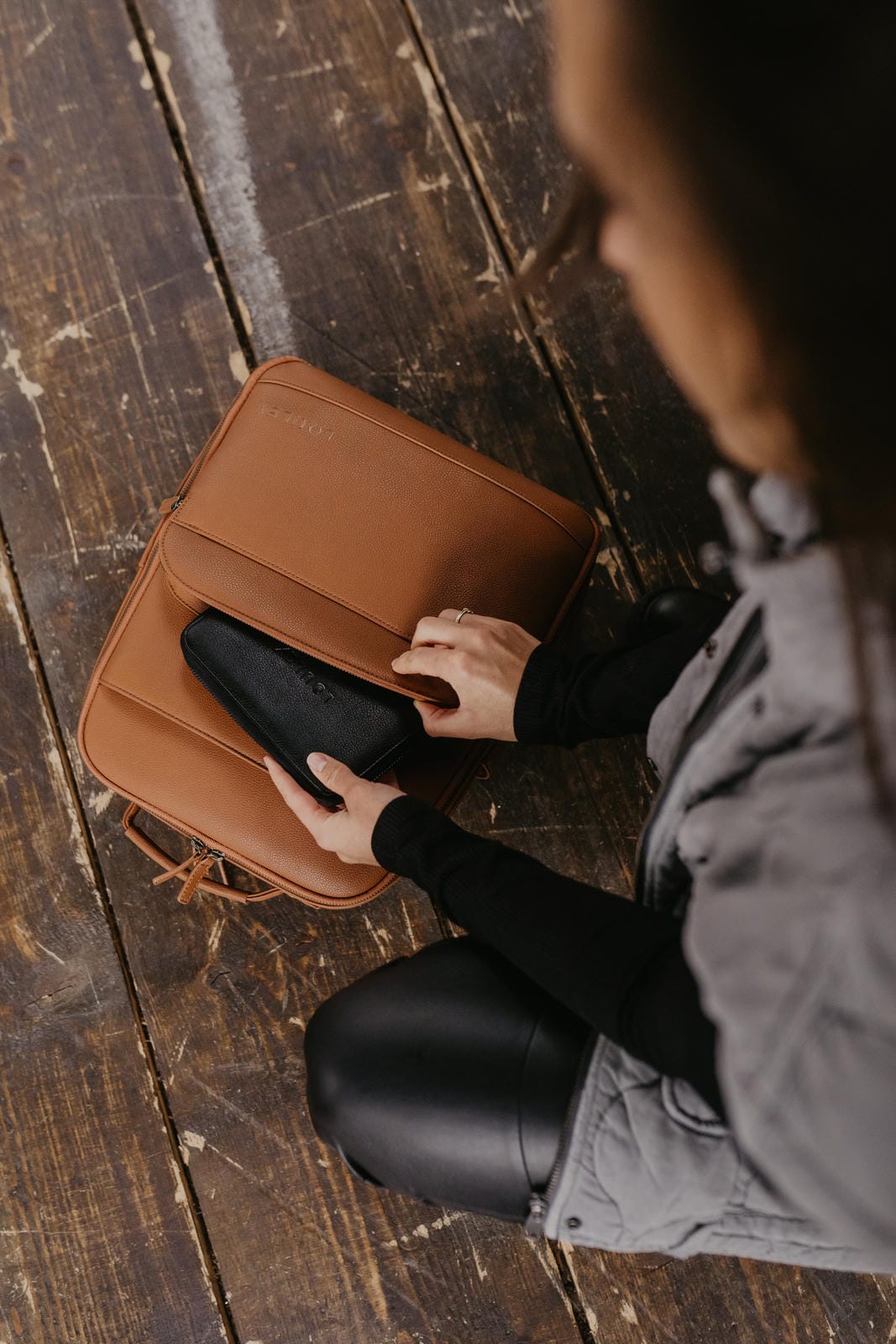 Person holding a brown leather bag on a wooden floor