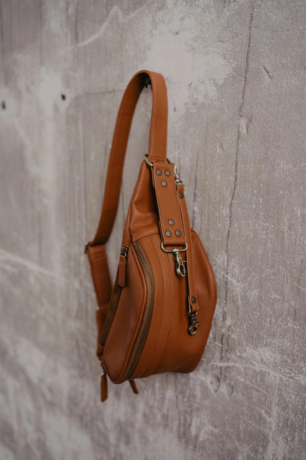 Brown leather sling bag on a textured gray background