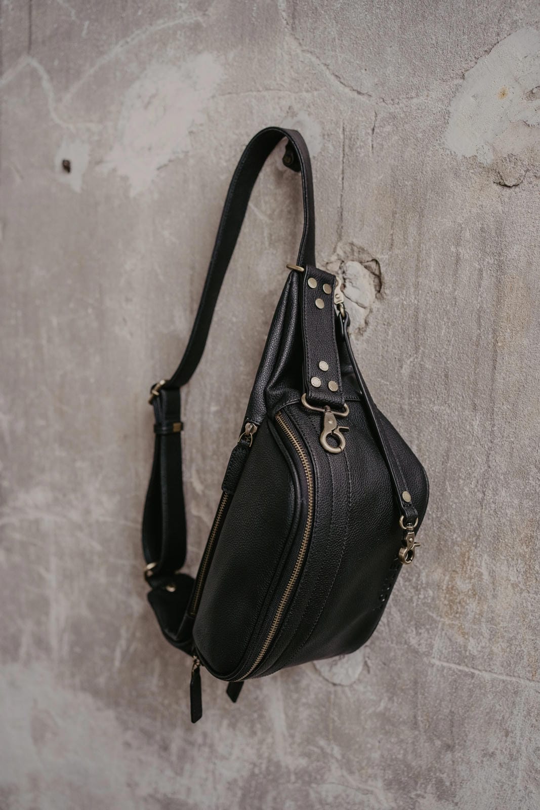 Black leather sling bag on a textured gray surface