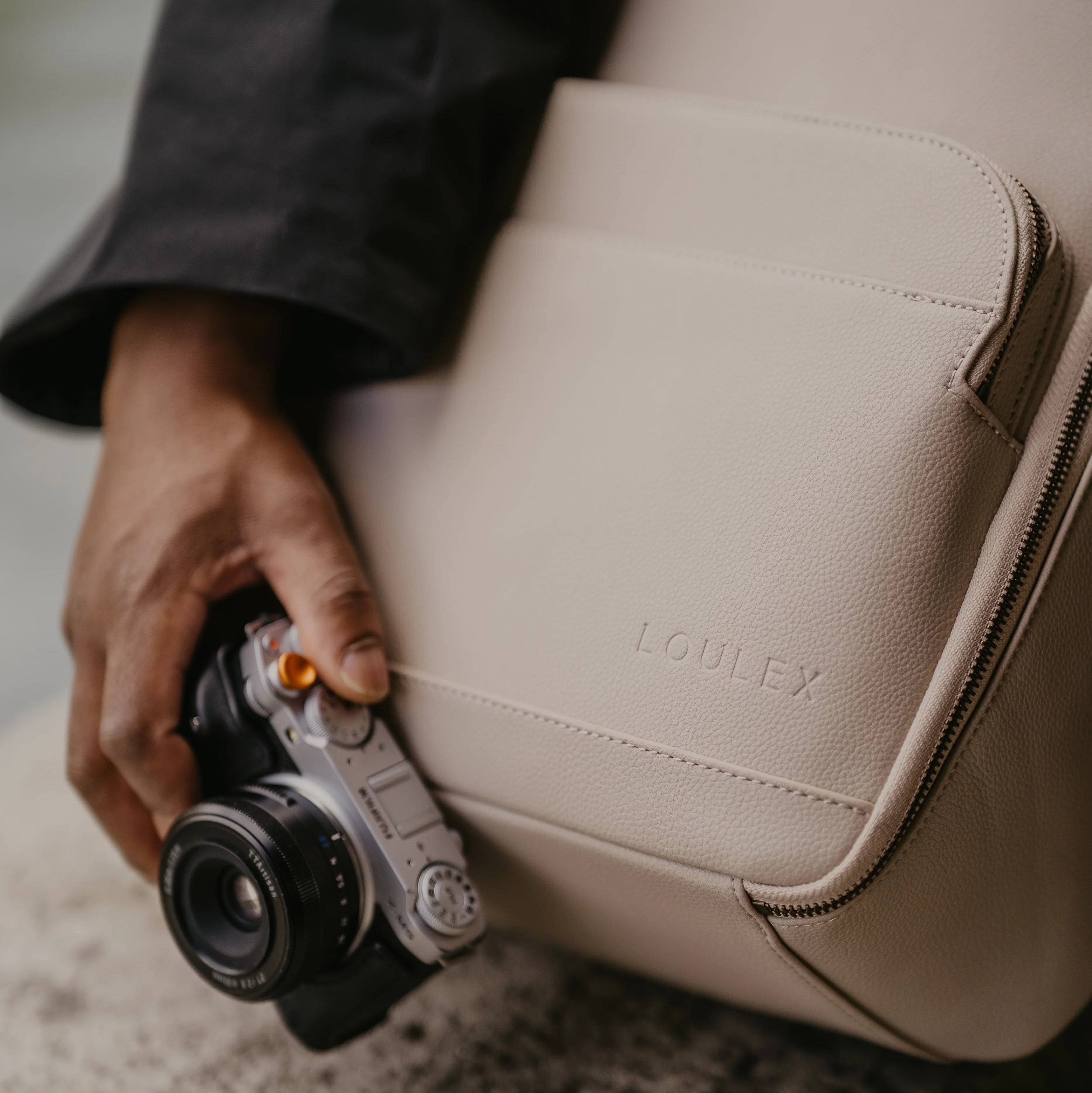 Person holding a beige leather bag with 'LOULEX' branding and a camera.