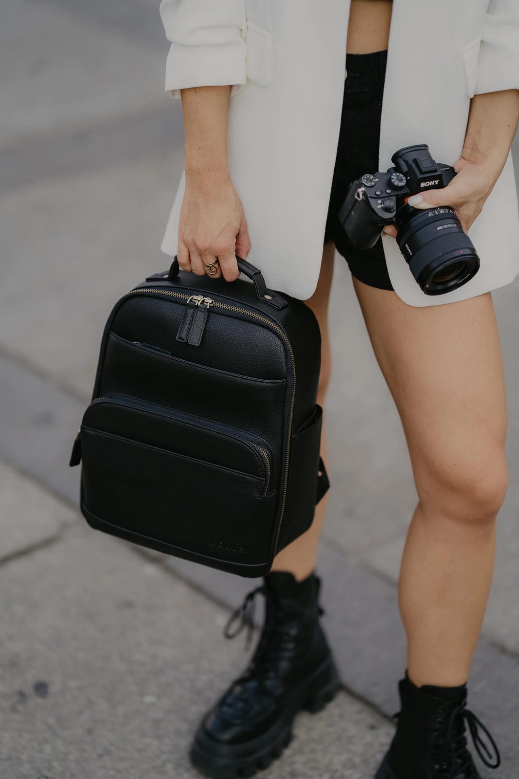 Person holding a black backpack and camera on a sidewalk