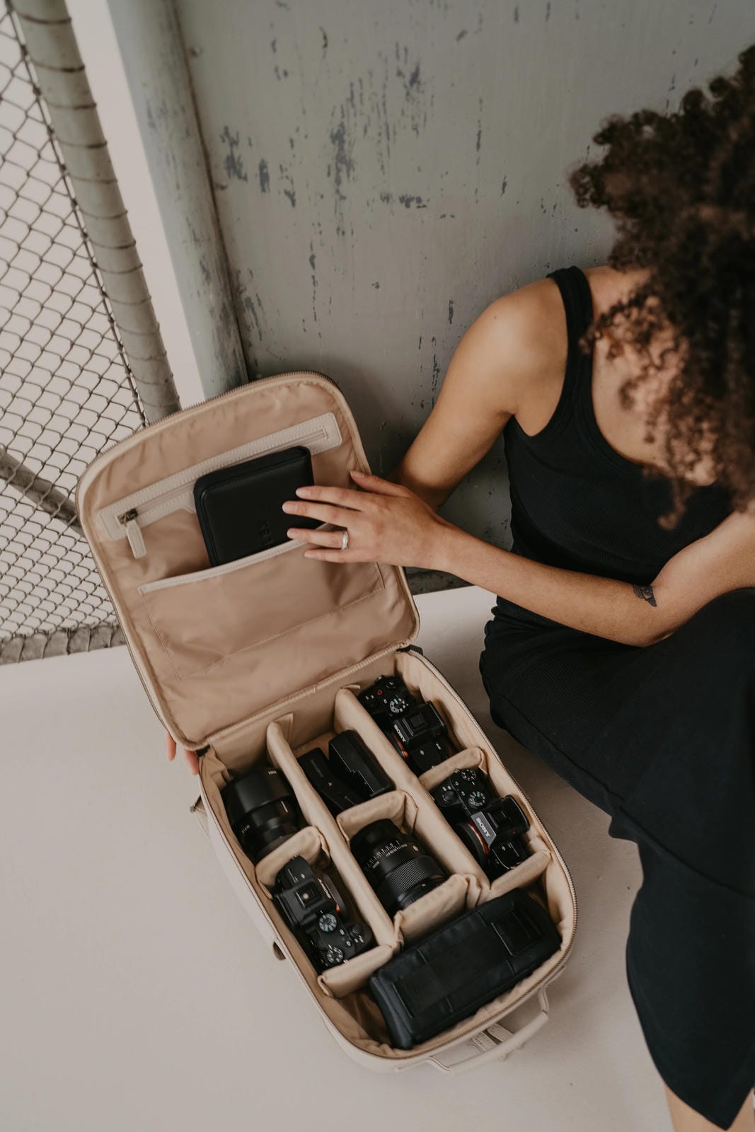 Person organizing camera equipment in a beige carrying case.