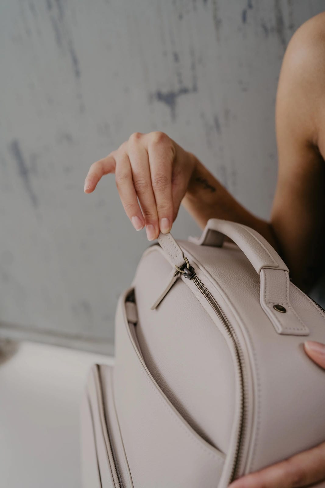 Person holding a light-colored handbag against a neutral background