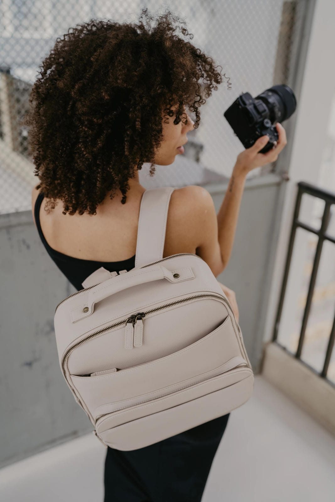 Woman holding a camera and wearing a beige backpack indoors.