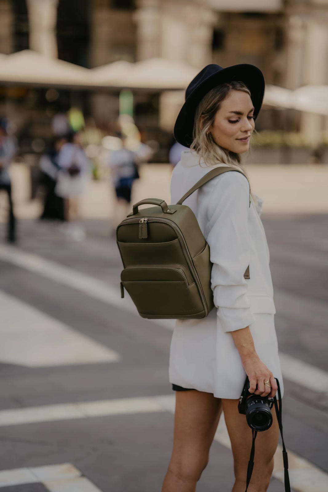 Woman with a green backpack and camera, walking on a street.