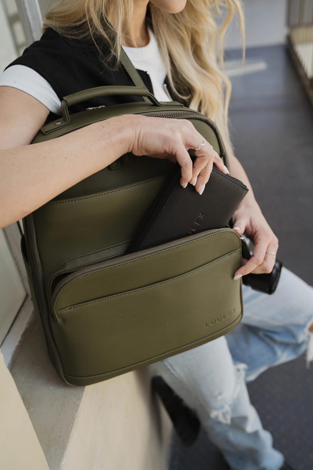 Person holding a green backpack with a black item inside, sitting on a bench.