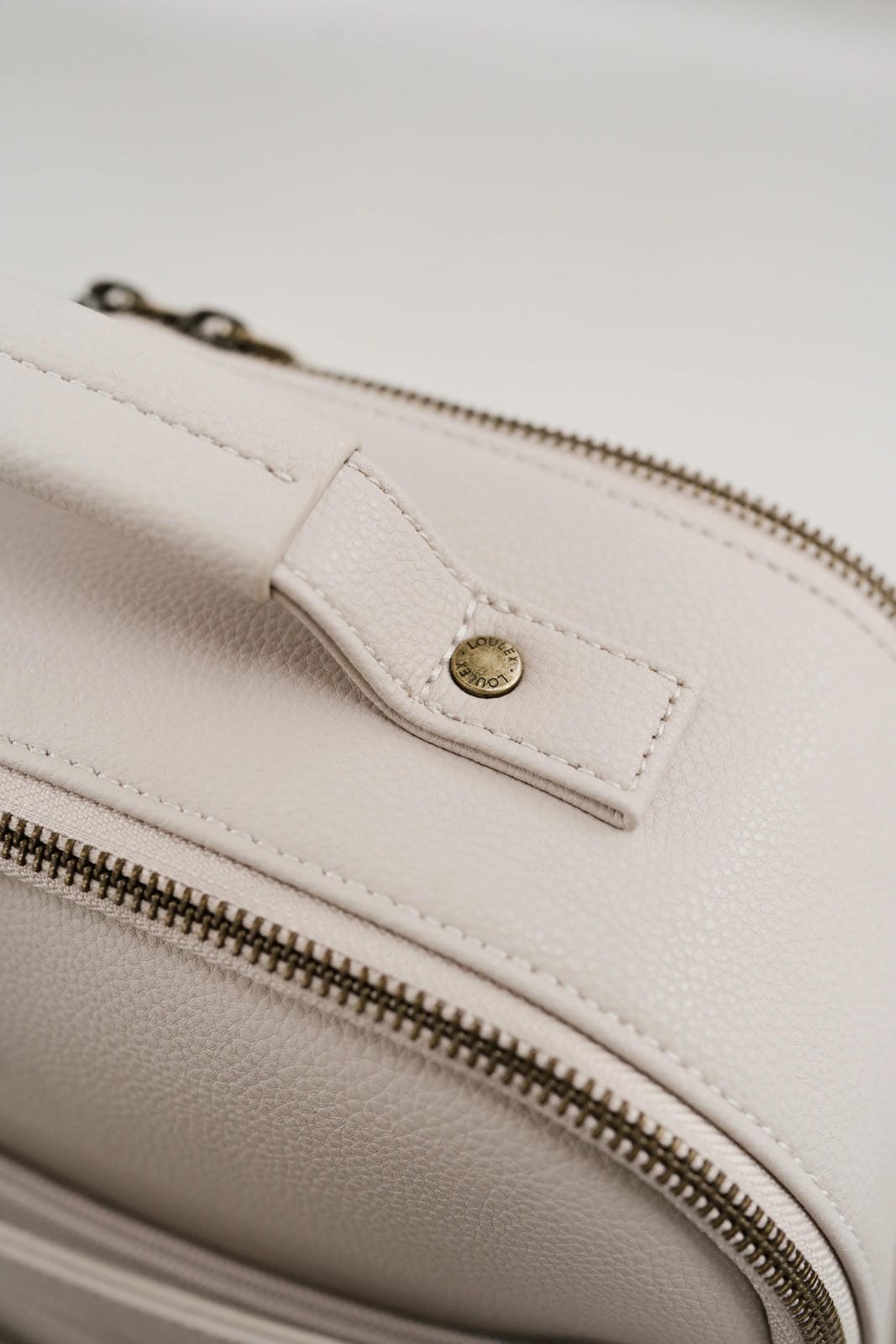 Close-up of a beige leather bag with a zipper and gold button detail.