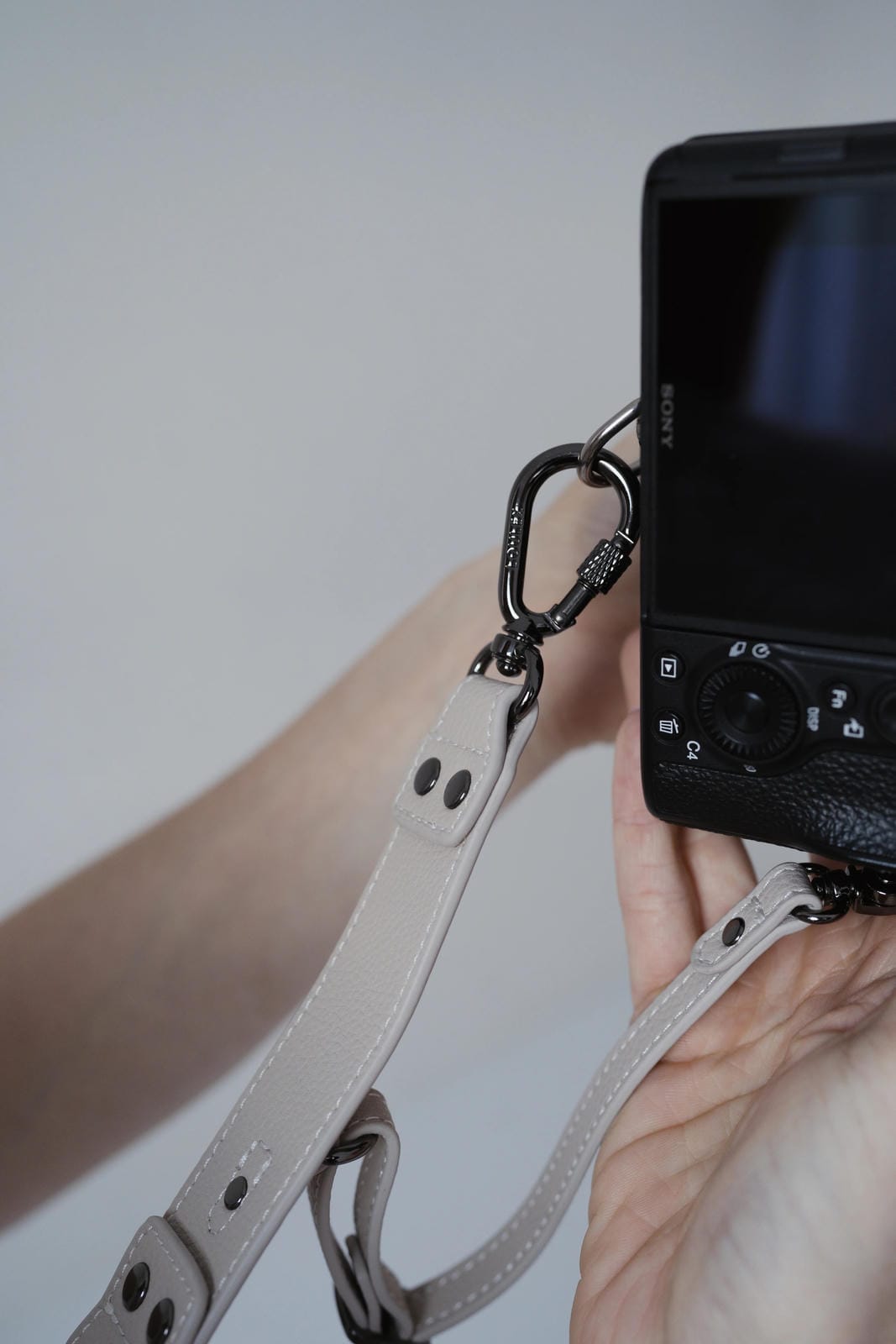 Person holding a camera with a beige leather strap against a plain background