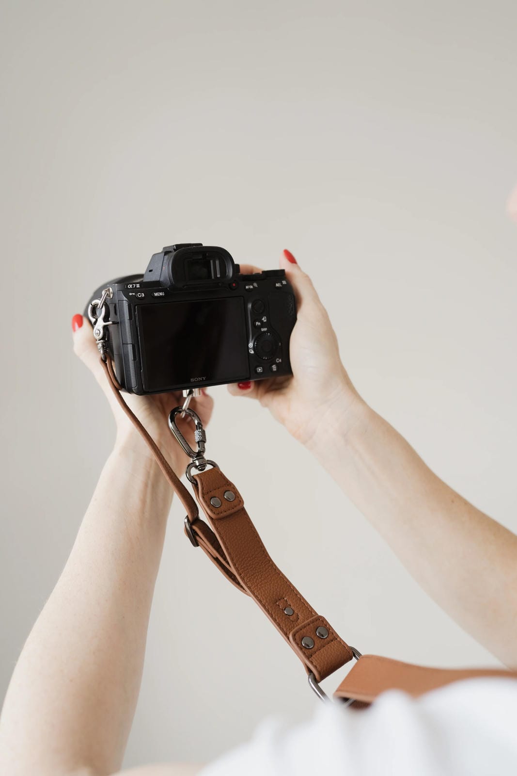 Person holding a camera with a brown strap against a plain background