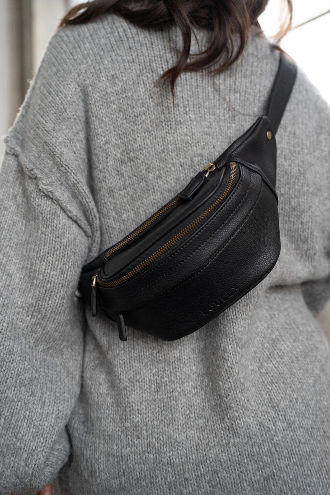 Person wearing a black waist bag over a gray sweater