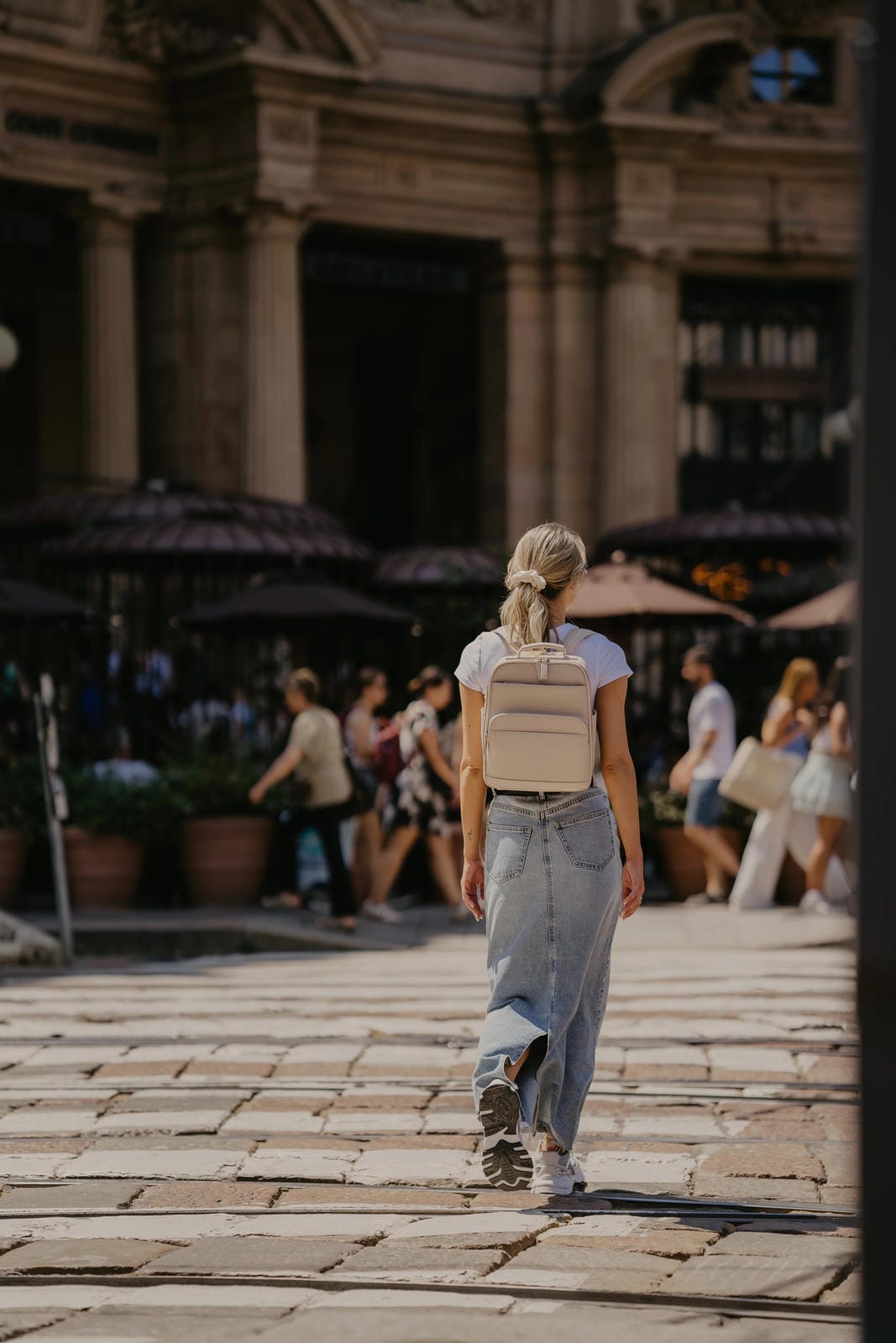 Person walking on a stone pavement with classical architecture in the background