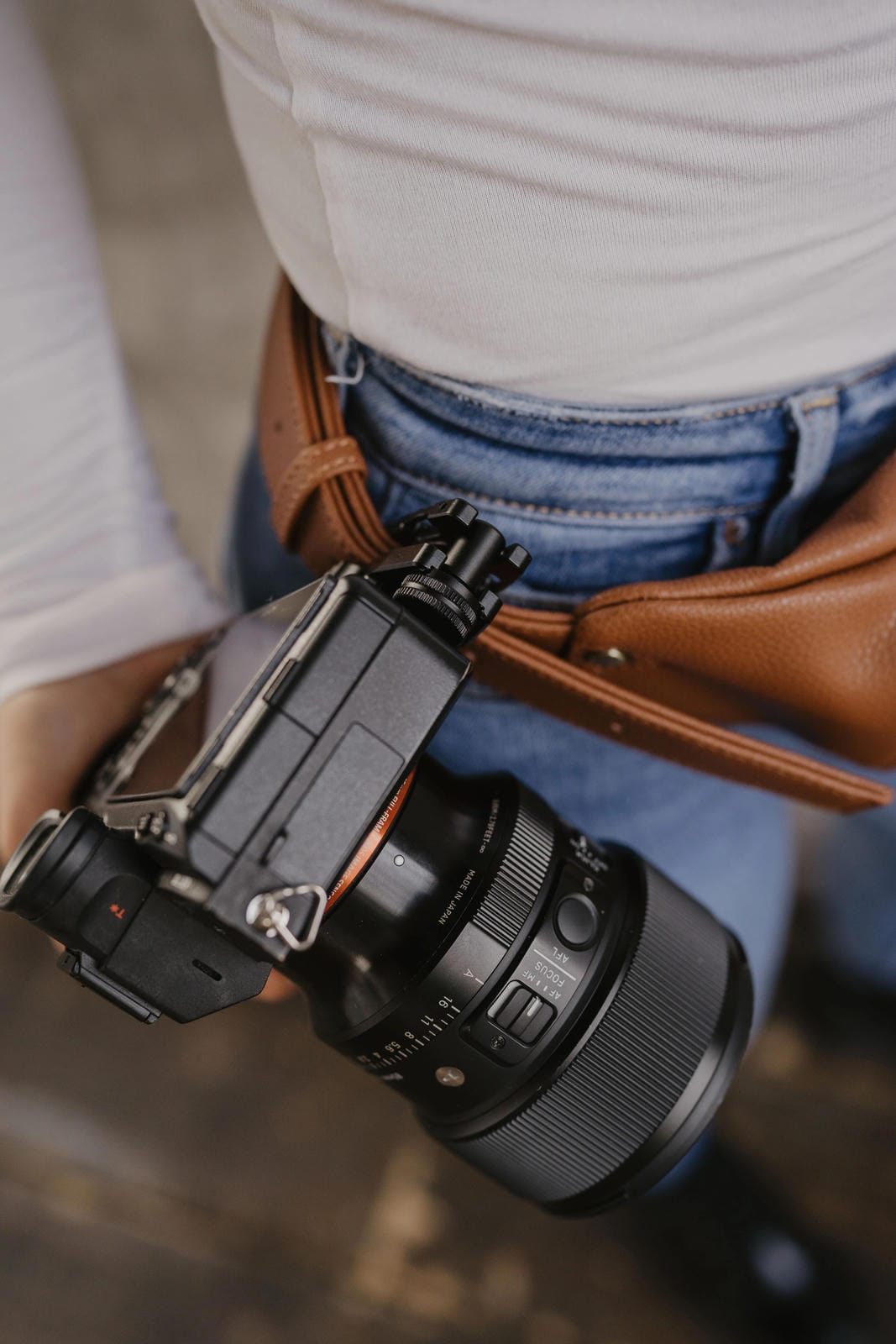 Person holding a camera with a lens attached, wearing a white shirt and blue jeans.