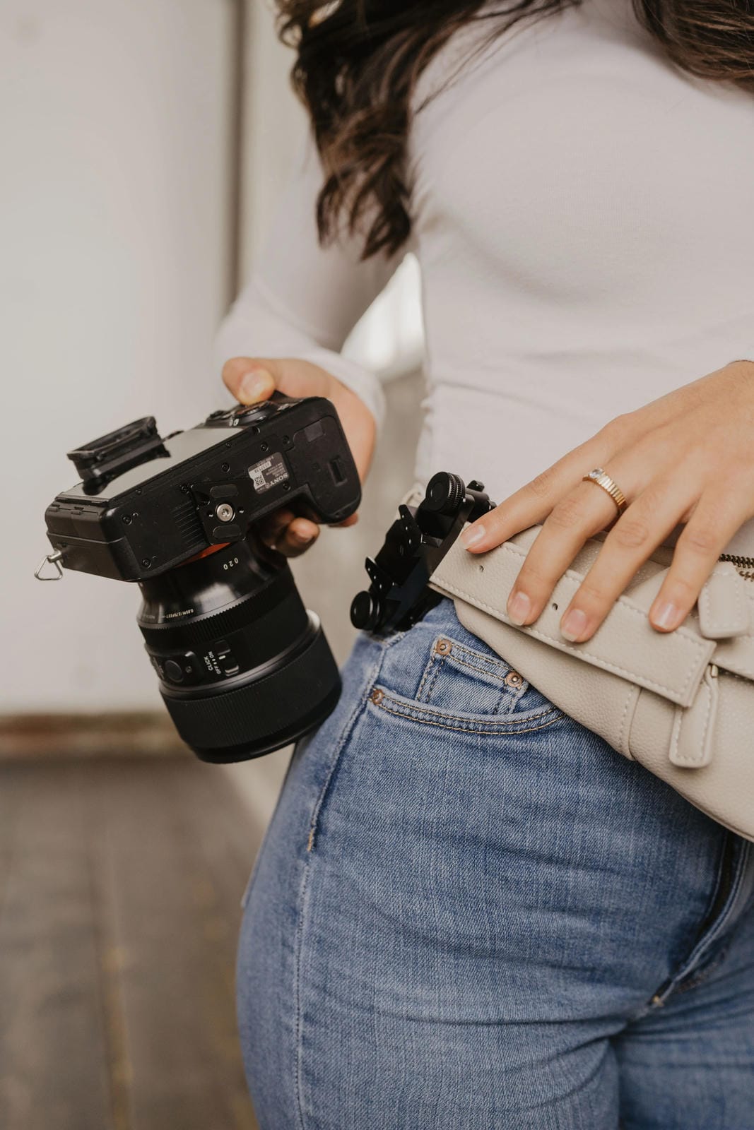 Person holding a camera with a lens, wearing a white shirt and blue jeans.
