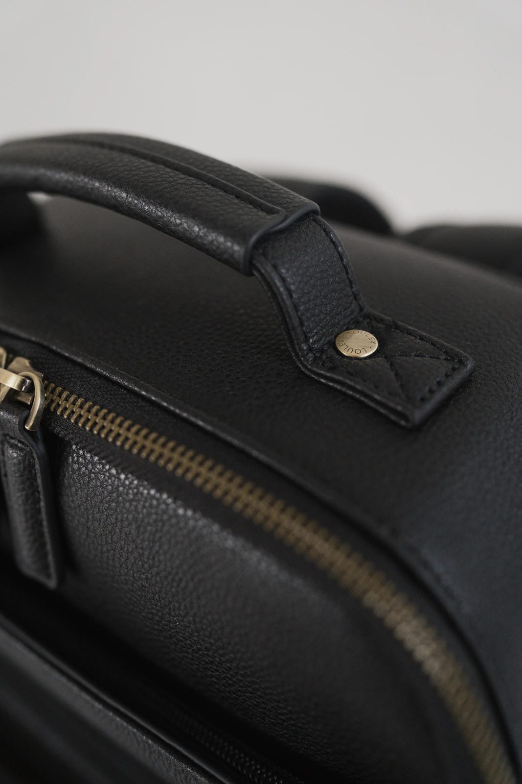 Close-up of a black leather bag with gold zipper and hardware.