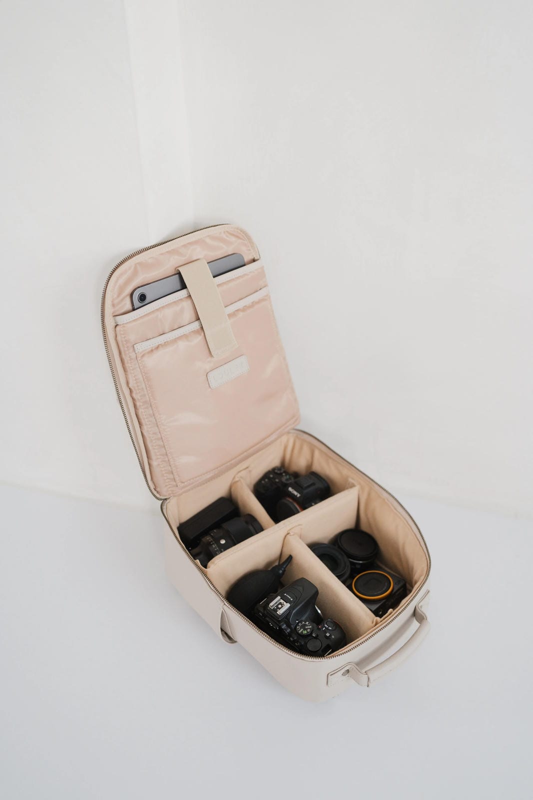 Beige travel case with compartments for electronic devices on a white background