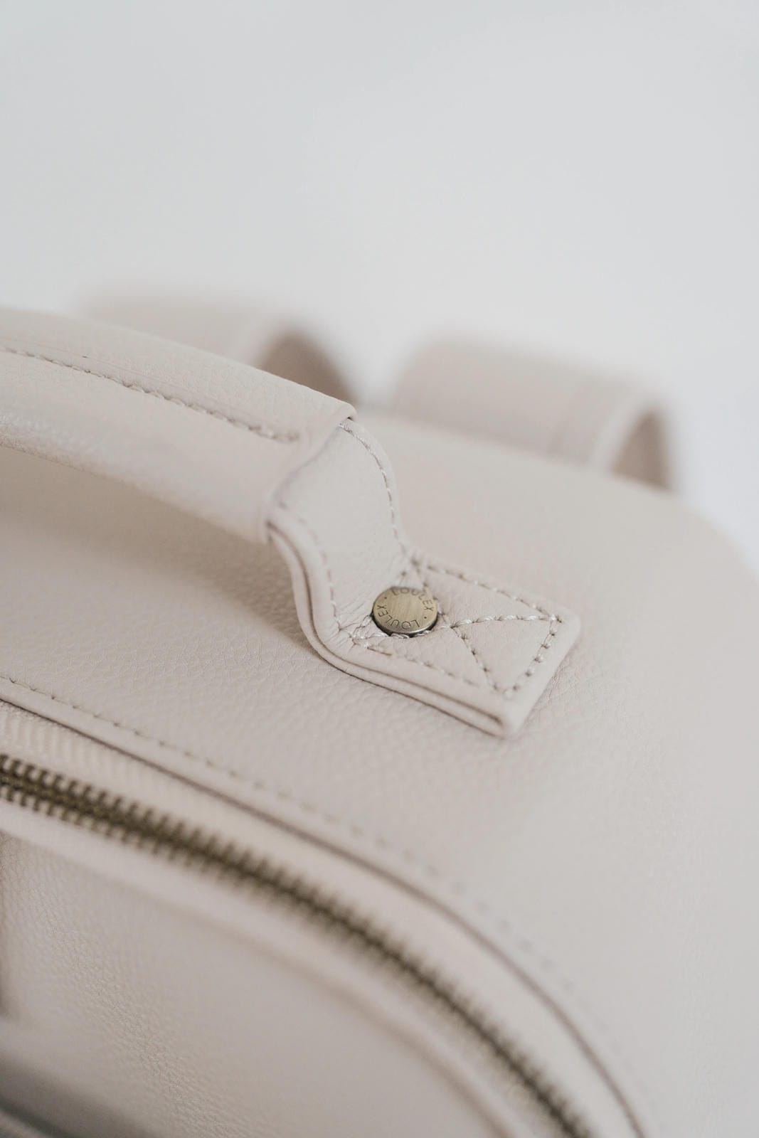 Close-up of a beige leather bag with a zipper on a light background