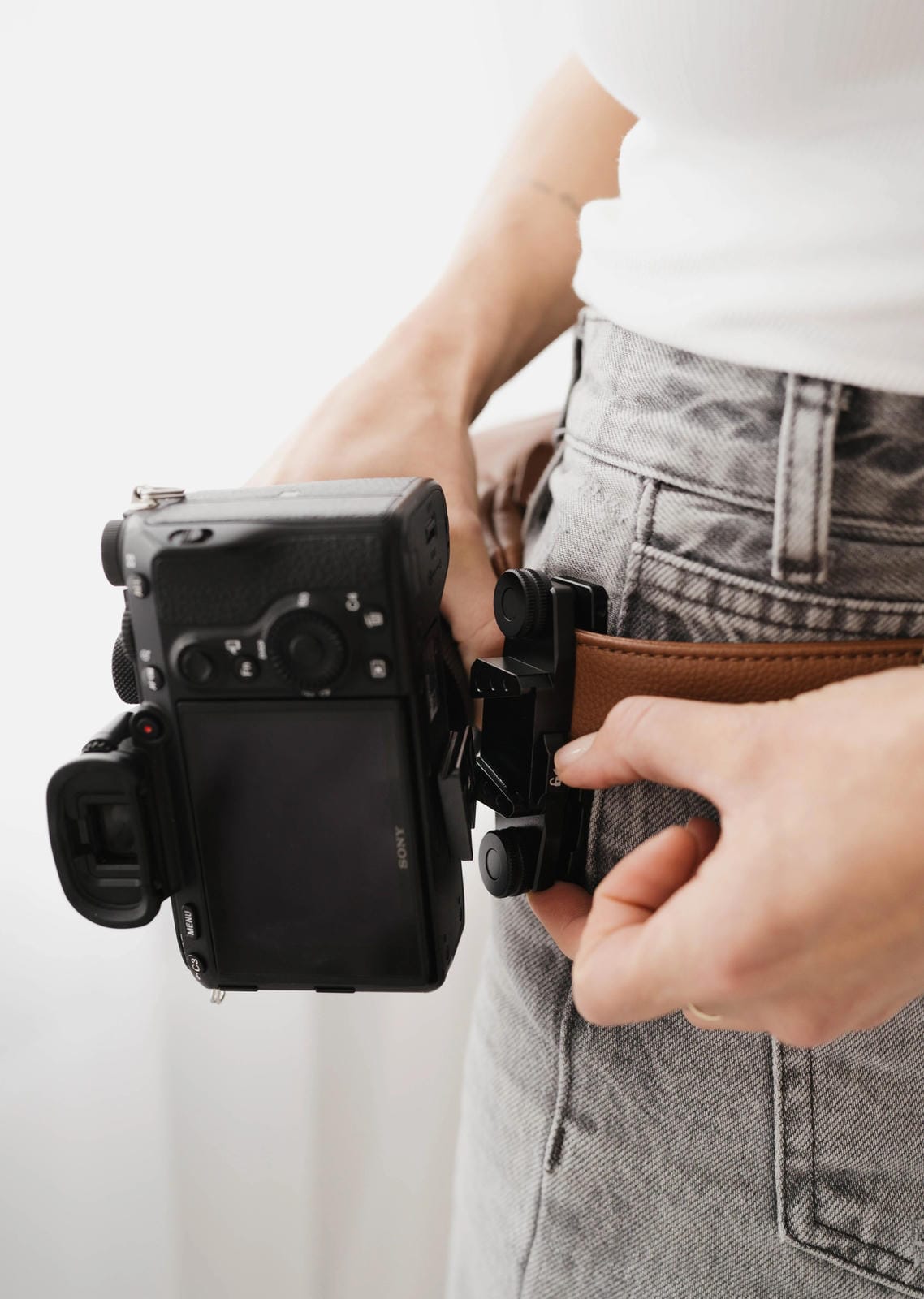 Person holding a camera with a strap over their shoulder against a white background