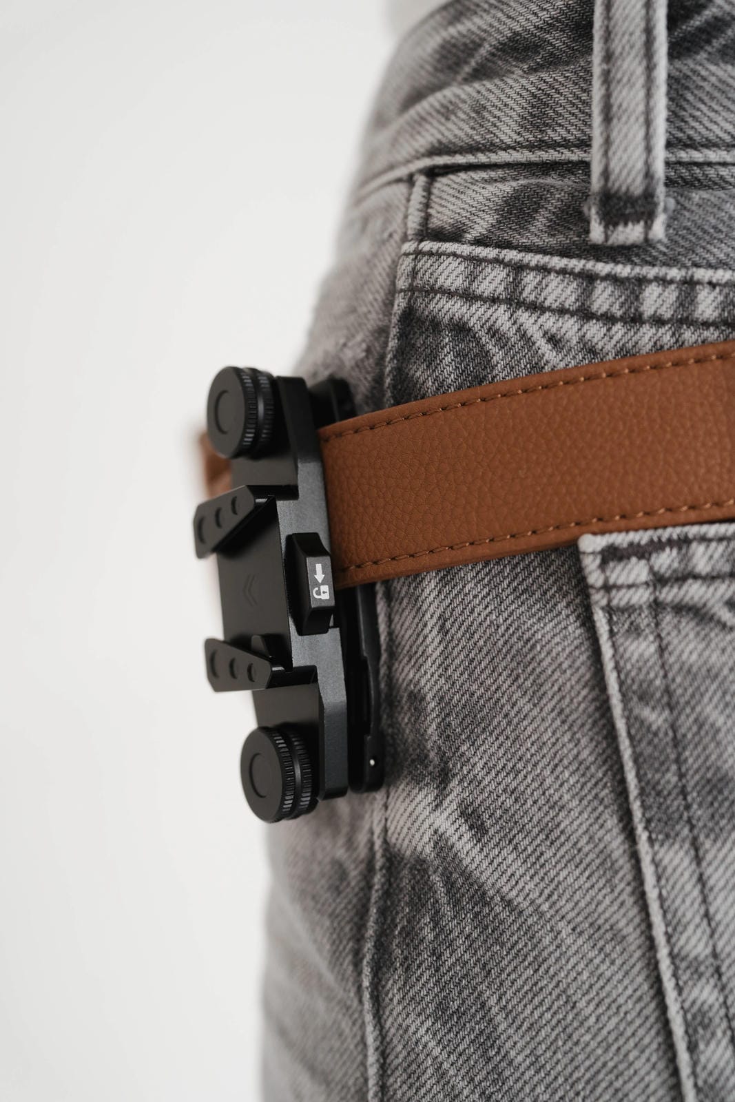 Close-up of a brown belt with a black buckle on gray pants against a white background