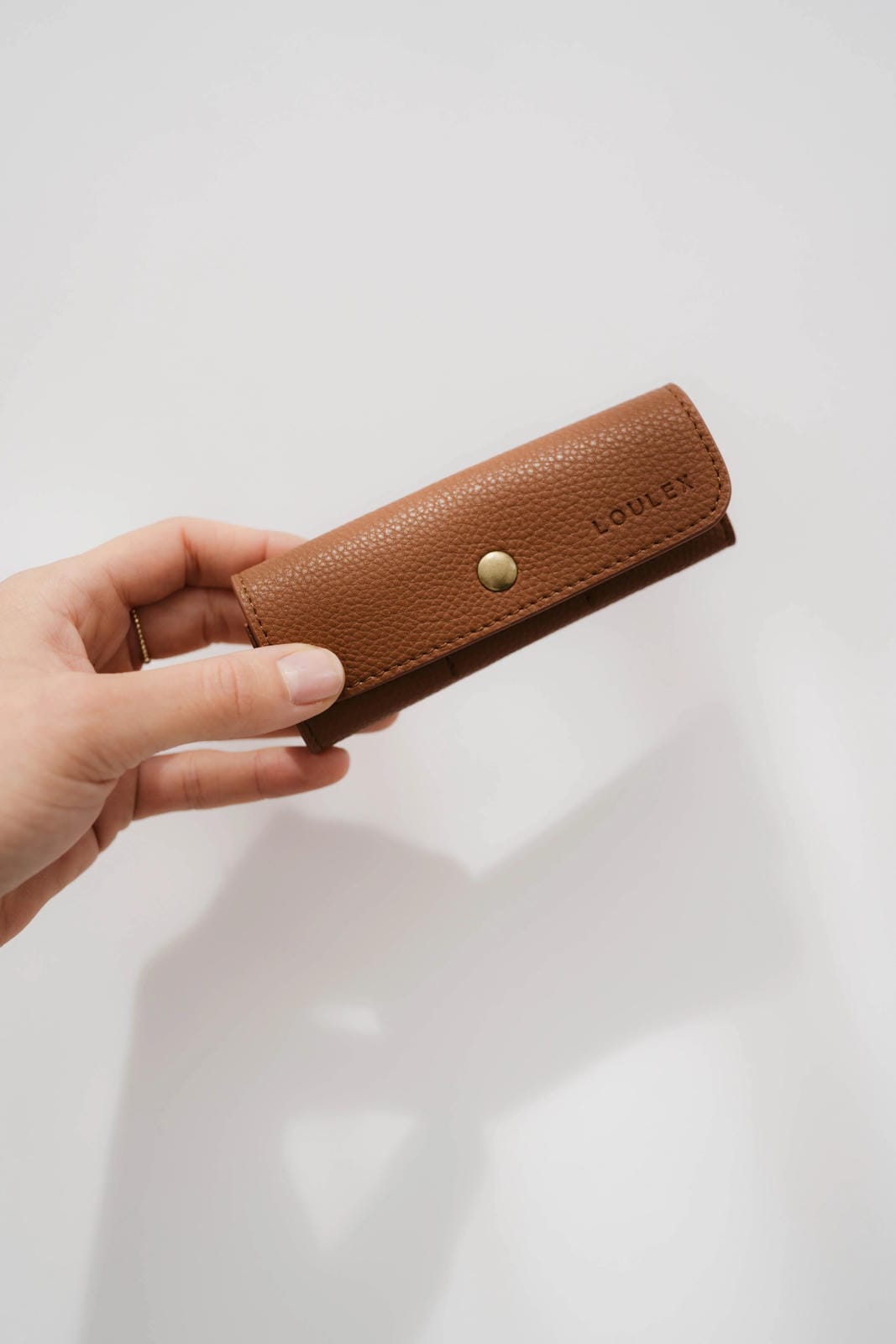 Hand holding a brown leather wallet with a visible brand logo on a light background