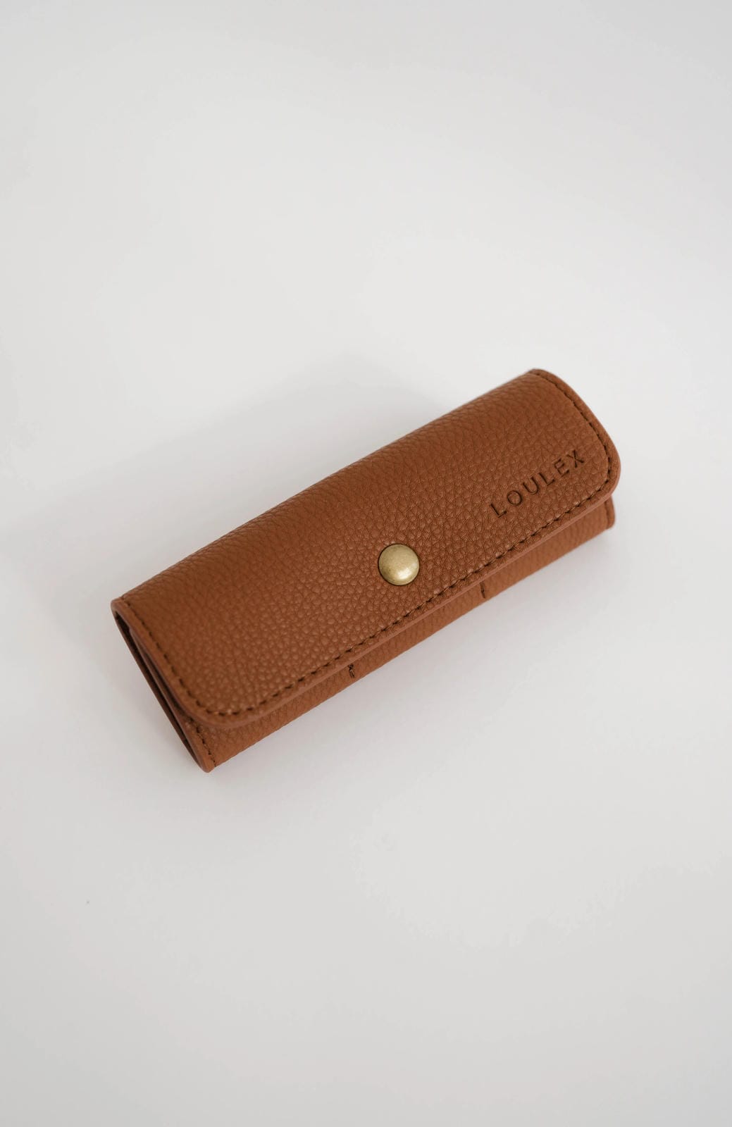Brown leather pencil case with a gold button on a white background