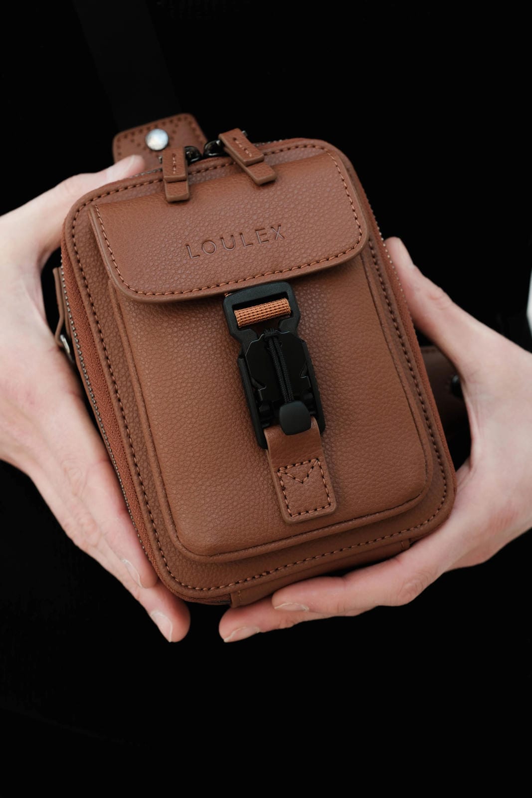 Brown leather pouch held by hands with a black background